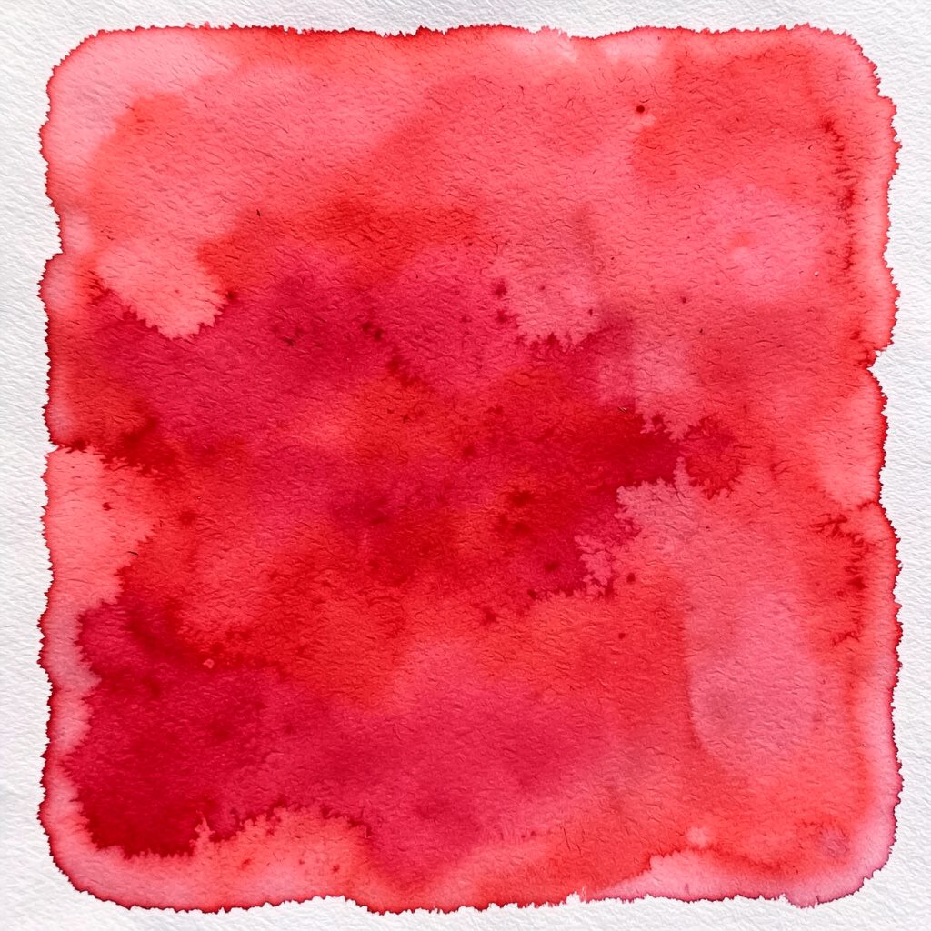 Soft watercolour-style quilt in rows of warm red, cream, and navy patchwork squares laid flat, cozy and homespun mood